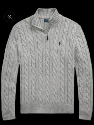 Ljusgrå kabelstickad tröja Polo Ralph Lauren - Säljer en ljusgrå kabelstickad tröja från Polo Ralph Lauren med halv dragkedja och hög krage. Tröjan har ribbade muddar och nederkant samt den klassiska broderade loggan på bröstet. Perfekt för dig som gillar stilren och tidlös design.