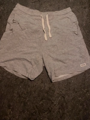 Grå mjukisshorts från Denim Makers - Mysiga grå mjukisshorts från Denim Makers med snörning i midjan och två fickor fram. Perfekta för chill dagar eller träning. Tillverkade i mjukt bomullsmaterial för extra komfort.