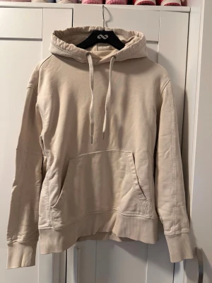 Beige hoodie från Calvin Klein - Snygg beige hoodie från Calvin Klein med broderad CK-logga på huvan. Hoodien har en stor känguruficka framtill, ribbade muddar vid ärmar och nederkant samt justerbar dragsko i huvan. Tillverkad i mjukt bomullsmaterial för skön känsla.