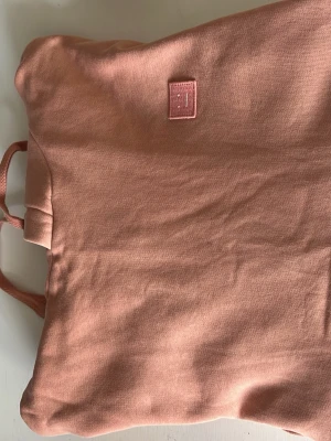 Rosa hoodie från Acne Studios - Säljer en snygg rosa hoodie från Acne Studios med klassisk huva och dragsko. Tröjan har en känguruficka framtill och det ikoniska Acne Studios-logotypen i form av ett litet ansikte på bröstet. Tillverkad i mjuk bomull för skön känsla.