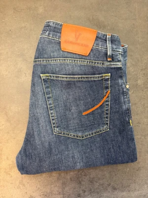 Handpicked Ravello Jeans, stl 35 - Snygga blå jeans från Handpicked med klassisk femficksdesign och en unik orange detalj på bakfickan. Jeansen har en rak passform och är tillverkade i slitstark denim med kontrastsömmar och läderpatch bak i midjan.