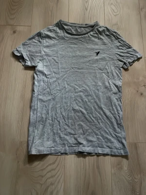 Ljusgrå t-shirt från Pier One - En basic ljusgrå t-shirt från Pier One i mjuk bomull. T-shirten har korta ärmar, rund halsringning och en liten svart logga på bröstet. Perfekt till jeans eller shorts för en enkel och clean look.