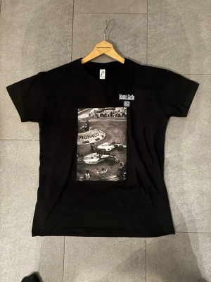Svart t-shirt med Monte Carlo-tryck - Cool svart t-shirt  med ett stort svartvitt tryck av Monte Carlo 1989 på bröstet. Klassisk passform med rund hals och korta ärmar. Perfekt för dig som gillar motorsport och retrostil.   Tröjan finns i storlek S M och L 