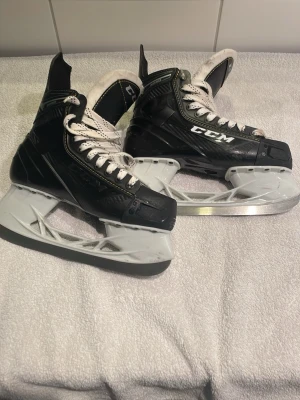hockeyskridskor från CCM stl.40,5 - Säljer ett par svarta hockeyskridskor från CCM med vita snören och gula detaljer. Skridskorna har robust form, högt skaft och klassisk design. Bra skick med någon enstaka repa.