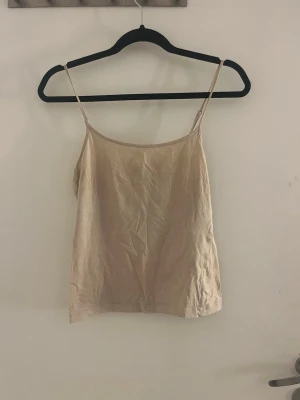 Beige linnetopp med tunna axelband - Snygg beige linnetopp med tunna axelband och enkel, rak passform. Perfekt att styla med jeans eller kjol för en clean look. Tillverkad i mjukt bomullsmaterial som känns skönt mot huden.