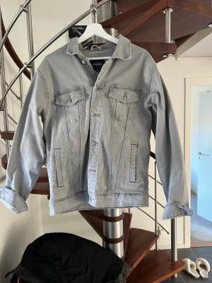 Ljusgrå jeansjacka från Dressmann - Snygg ljusgrå jeansjacka från Dressmann i klassisk modell med två bröstfickor med lock och knappar samt två sidofickor. Rak passform och stilrena sömmar. Perfekt för dig som vill ha en enkel men trendig jacka till vardagslooken.