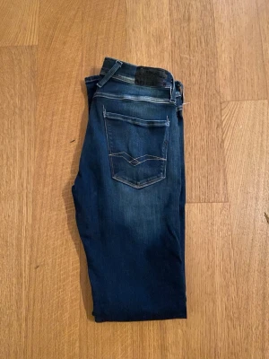 Replay anbass - Snygga mörkblå Replay anbass jeans med slitningar och ljusare partier på låren. Klassisk femficksmodell med kontrastsömmar och låg midja. Perfekta för en trendig och avslappnad stil.