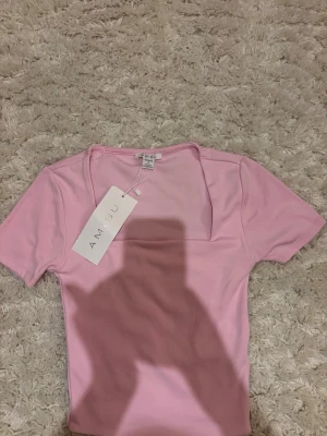 Ljusrosa topp från Amisu - Säljer en ljusrosa topp från Amisu med korta ärmar och fyrkantig ringning. Toppen är i ett mjukt, stretchigt material och har en slim passform som sitter snyggt på kroppen. Perfekt att styla med jeans eller kjol.