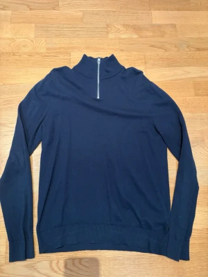 Mörkblå stickad halfzip  - Mörkblå stickad tröja med lång ärm och hög krage med halv dragkedja framtill från Jack & Jones. Tröjan har ribbade muddar vid ärmslut och nederkant. Perfekt för lager på lager och enkel att matcha till olika outfits. Storlek M. Tveka inte på att höra av dig vid frågor eller funderingar kring passform eller annat. 