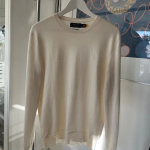 Vit stickad tröja Polo Ralph Lauren - Klassisk cremevit stickad tröja från Polo Ralph Lauren i slim fit-modell. Tillverkad i mjuk och tvättbar merinoull med rund halsringning och diskret broderad logga på bröstet. Perfekt för en stilren och clean look.