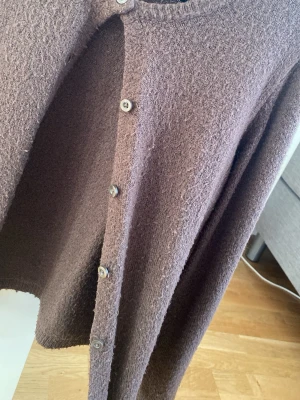 Brun kofta från 157 med knappar - Mysig brun kofta från 157 med rund halsringning och knäppning framtill. Tillverkad i ett mjukt, stickat material som känns skönt mot huden. Perfekt för lager på lager och enkel att matcha med olika outfits.