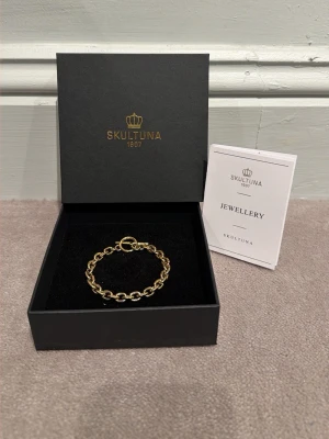 Guld kedjearmband Skultuna - Nypris: 1000Snyggt guld armband från Skultuna med klassisk kedjedesign och elegant T-låsfäste. Armbandet kommer i original ask. Perfekt accessoar för dig som gillar stilrena smycken med exklusiv känsla.