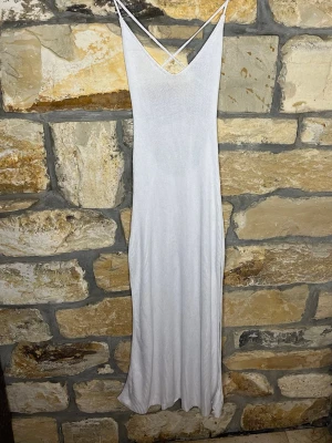 Vit långklänning med smala axelband - stilren vit långklänning med smala axelband som korsas i ryggen. Klänningen har en v-ringad front och är tillverkad i ett ribbat material som ger en snygg passform. Perfekt för sommarens alla tillfällen!