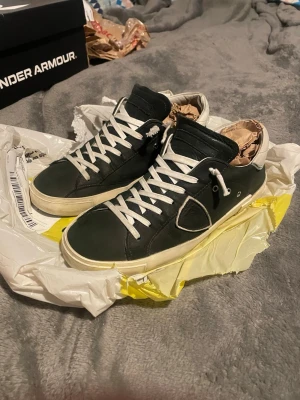 Philippe Model skor - Stilrena svarta sneakers från Philippe Model med vita skosnören och vit sula. Skorna har en klassisk låg profil och är tillverkade i läder med diskreta logodetaljer på sidan. Perfekta för en trendig och avslappnad look. Storlek 42