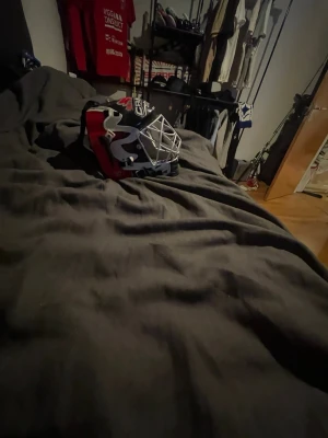 Ishockeymålvaktsmask Bauer svart/röd canada  - Säljer en cool ishockeymålvaktsmask från Bauer i svart, rött och vitt. Masken har ett klassiskt galler i metall och snygg design med logga på sidan. Perfekt för dig som vill sticka ut på isen och skydda ansiktet under match eller träning. Det är en canada hjälm 