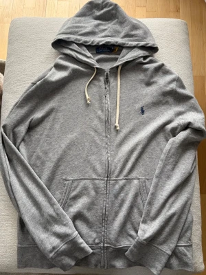 Spa Terry Full Zip Hoodie från Polo Ralph Lauren - Grå hoodie med dragkedja från Polo Ralph Lauren. Klassisk design med huva och vita dragsnören, känguruficka framtill och broderad logga på bröstet. Tillverkad i mjuk bomullsblandning för skön känsla. Vid frågor eller fler bilder kontakta mig privat så hjälper jag gärna till😁