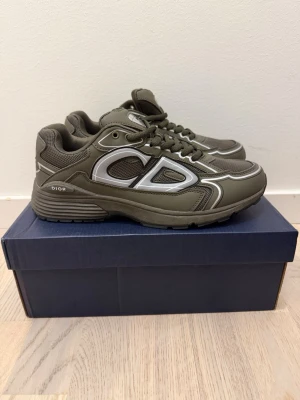 Olivgröna Dior sneakers med meshdetaljer - Snygga olivgröna Dior sneakers med stora CD-detaljer i silver på sidan. Skorna har en chunky sula, meshpaneler för extra ventilation och coola kontrastsömmar. Klassisk snörning och logga på plösen. Perfekta för dig som vill sticka ut med stilrena och exklusiva sneakers. Aldrig använda.