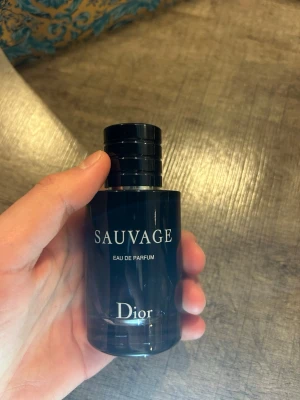Dior Sauvage Eau de Parfum - Dior Sauvage Eau de Parfum är en ikonisk herrdoft i en elegant, mörkblå glasflaska med svart kork. Flaskan har en stilren, rund form och tydlig logga framtill. Doften är känd för sin fräscha och kryddiga karaktär, perfekt för dig som vill sticka ut. Ungefär 40 ml kvar av 60 ml 