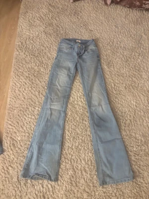 Ljusblå bootcut jeans  - Säljer ett par ljusblå Lågmidjade bootcut jeans med snygg broderad detalj i rosa på bakfickorna. Jeansen har klassisk femficksdesign och är tillverkade i denim med lätt tvättad look. 