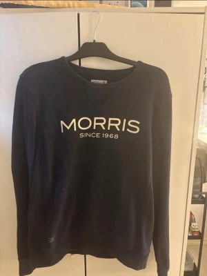 Svart sweatshirt från Morris - Snygg svart sweatshirt från Morris med vit logga 'MORRIS SINCE 1968' på bröstet. Tröjan har rund halsringning, långa ärmar och en liten patch på ärmen. Perfekt för en avslappnad och stilren look.