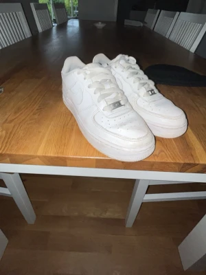 Vita Nike Air Force 1 sneakers - Klassiska vita Nike Air Force 1 sneakers i lågt utförande. Skorna har en chunky sula, perforerad tåbox och ikonisk Swoosh på sidan. Tillverkade i läder med vita skosnören och metall-detalj vid snörningen. Perfekta för en clean och stilren look. Skriv vid fundering\mer bilder.😀