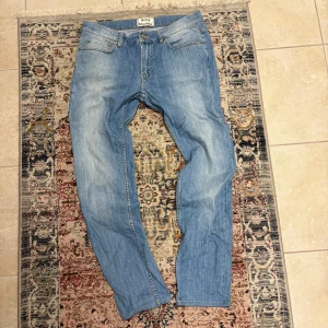 Ljusblå raka jeans från Acne Studios - Säljer ett par ljusblå jeans från Acne Studios med klassisk femficksmodell och raka ben. Jeansen har en rak passform och subtila slitningar framtill för en cool vintagekänsla. Finns 1 fläck på nedre delen av ena benet (bild 3) annars i väldigt bra skick.