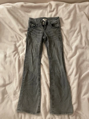Grå bootcut jeans med låg midja - Säljer ett par grå bootcut jeans med låg midja. Jeansen är en aning slitna och skrynkliga som ni kan se på bilderna.