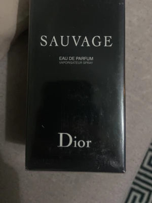 Dior Sauvage Eau de Parfum - Dior Sauvage Eau de Parfum är en lyxig herrdoft i en elegant svart kartong med vit text. Förpackningen har en stilren design och är tillverkad av kartong med plastfilm. Perfekt för dig som vill ha en ikonisk och modern parfym.