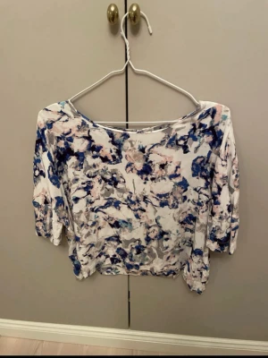 Blommig topp med trekvartsärm - Snygg topp med blommigt mönster i blått, rosa och vitt. Modellen har trekvartsärm och en lös passform med bred halsringning. Perfekt för dig som gillar färg och mönster i din garderob.
