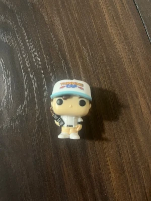 Funko Pop, Dustin - Säljer en Funko Pop figur med vit och blå keps där det står 'Thinking Cap', vit skjorta och gula byxor. Figuren håller i en liten svart detalj och har typisk Funko Pop-stil med stora ögon och huvud. Perfekt för samlare eller som dekoration.