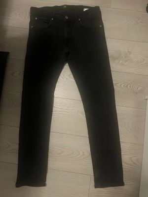 Svarta jeans från Lee - Snygga svarta jeans från Lee med klassisk femficksdesign och knappgylf. W34 L32