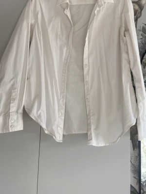Vit klassisk skjorta i bomull - Säljer en stilren vit skjorta med klassisk krage och knappar framtill. Skjortan har lång ärm och är tillverkad i mjuk bomull, perfekt för en clean och enkel look. Passar till allt och är ett måste i garderoben.