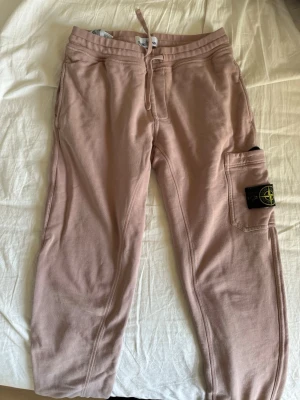 Beiga mjukisbyxor från Stone Island - Säljer ett par beiga mjukisbyxor från Stone Island med dragsko i midjan och en stor ficka på benet med den klassiska Stone Island-loggan. Byxorna är i mjukt bomullsmaterial och har avslappnad passform, perfekta för chill dagar.