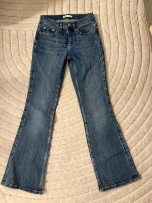 Blå bootcut jeans med utsvängda ben - Säljer ett par klassiska blå bootcut jeans i st 34(petit) med utsvängda ben och fem fickor. Jeansen har en låg midja och är tillverkade i denim. Perfekta för en avslappnad och trendig look.