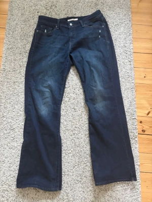 Levi's 529 Curvy Bootcut Jeans - Mörkblå Levi's 529 med bootcut. Otroligt fin tvätt och fin silhuett som sticker ut. Har små slitningar i tyget, se bild 4 & 5. Hör av er med frågor! 