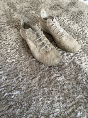 Vita fotbollsskor från Puma - Säljer ett par vita fotbollsskor från Puma med klassisk låg profil och snörning. Skorna har en tunn ovandel i textilmaterial och diskret Puma-logga på hälen. Perfekta för dig som vill ha lätta och smidiga skor på planen.