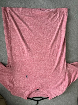 Rosa t-shirt från Ralph Lauren - Säljer en rosa t-shirt från Ralph Lauren med klassisk v-ringning och den ikoniska broderade loggan på bröstet. T-shirten är kortärmad och gjord i mjuk bomull, perfekt för en avslappnad stil.