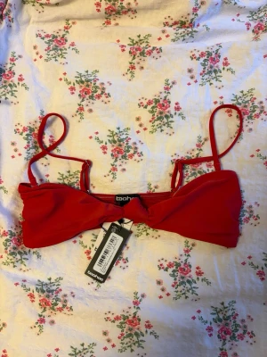 Röd bikiniöverdel från Boohoo - Snygg röd bikiniöverdel från Boohoo med smala axelband och twistad detalj framtill. Justerbara och avtagbara axelband för perfekt passform. Perfekt för sommardagar på stranden eller vid poolen. Nypris: 265kr
