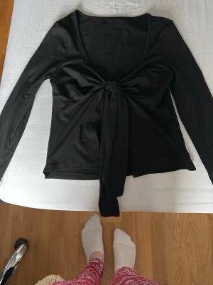 Svart omlottopp med knyt framtill - Stilren svart omlottopp med långa ärmar och knyt framtill. Tillverkad i mjuk och stretchig polyesterblandning som sitter snyggt på kroppen. Perfekt att matcha med både jeans och kjol för en trendig look. Tröjan är från SHEIN 