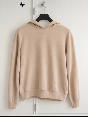Beige hoodie med luva - En stilren beige hoodie med luva och långa ärmar. Hoodien har en avslappnad passform och ribbade muddar vid ärmslut och nederkant. Perfekt för en chill och enkel look. Materialet känns mjukt och bekvämt mot huden.