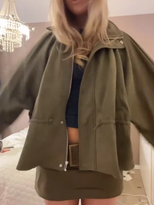 Olivgrön loose jacka med dragkedja  - Snygg olivgrön jacka i loose passform med dragkedja framtill och stora ärmar. Jackan har en enkel design med knappar och hög krage. Perfekt för dig som gillar en avslappnad och trendig stil.