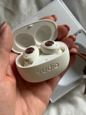 Sudio vita trådlösa in-ear hörlurar - De extra öronpropparna finns ej med!! Snygga vita trådlösa in-ear hörlurar från Sudio med matchande laddningsetui. Hörlurarna har en stilren design med bruna detaljer på toppen och ett smidigt fodral med präglad logga och läderrem. Perfekta för musik, poddar och samtal på språng.