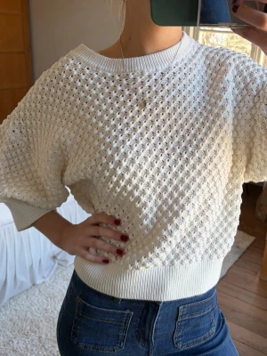 Vit kortärmad stickad tröja - Säljer en vit stickad tröja med korta ärmar och bred ribbad mudd i midjan och vid ärmsluten