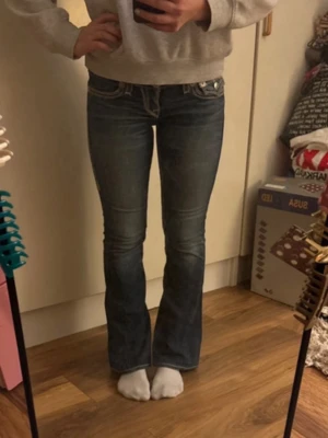 True Religion bootcut jeans  - Säljer ett par True Religion blå bootcut jeans. Jeansen har låg midja, klassiska fem fickor och detaljerade sömmar. Perfekta för en avslappnad och trendig look. Jättesnygga!