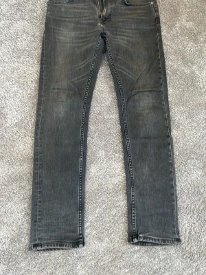 Nudie jeans Lean Dean - Säljer ett par grå jeans med tvättad look och raka ben. Jeansen har klassiska fem fickor och subtila slitningar på både fram- och baksida för en avslappnad stil. Materialet är denim i bomull och passformen är normal. 30/30