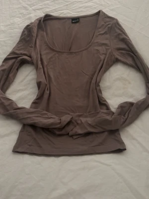 Beige långärmad topp Gina Tricot - Säljer en enkel och stilren beige långärmad topp från Gina Tricot. Toppen har en rund, djupare urringning och är gjord i mjukt material som sitter skönt mot kroppen. Perfekt att matcha med jeans eller kjol för en clean look.