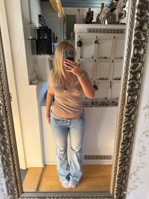 Beige topp med v-ringning och ringdetalj - Säljer en beige topp från Gina Tricot med korta ärmar och snygg v-ringning. Toppen har en ringdetalj framtill med rynkade veck som ger en cool twist. Tillverkad i mjuk bomullsmix och sitter normal på kroppen. Perfekt till jeans eller kjol!