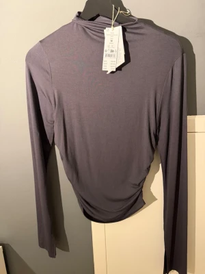 Mörkgrå långärmad polotopp - Säljer en stilren mörkgrå polotopp med lång ärm. Toppen har en tight passform och är tillverkad i ett mjukt, stretchigt material som känns skönt mot huden. Perfekt att matcha med jeans eller kjol för en clean look.