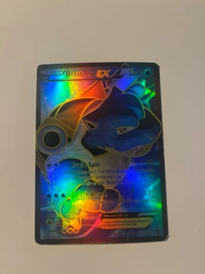Pokémonkort Blastoise EX holo - Säljer ett Blastoise EX holografiskt samlarkort från Pokémon. Kortet har en färgstark holoeffekt och visar Blastoise med attacker som Rapid Spin och Splash Bomb. Perfekt för samlare eller Pokémonfans som vill utöka sin kortsamling. Notera att kortet är lite ”skrapat” i hörnen (se bild 3) kortet är värderat till 141 dollar. 