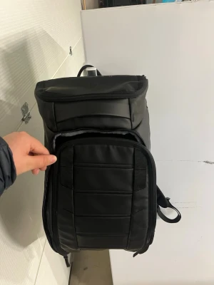 Svart stilren ryggsäck med vaddering - Snygg svart ryggsäck med vadderade axelband och flera fack. Ryggsäcken har en modern, rektangulär form och är tillverkad i ett slitstarkt, vattenavvisande material. Perfekt för dig som vill ha en clean och praktisk väska till skolan eller stan köpte den för 2200kr men säljer den för 500kr för tragketja är trasigt och lite till som man ser på bilden.